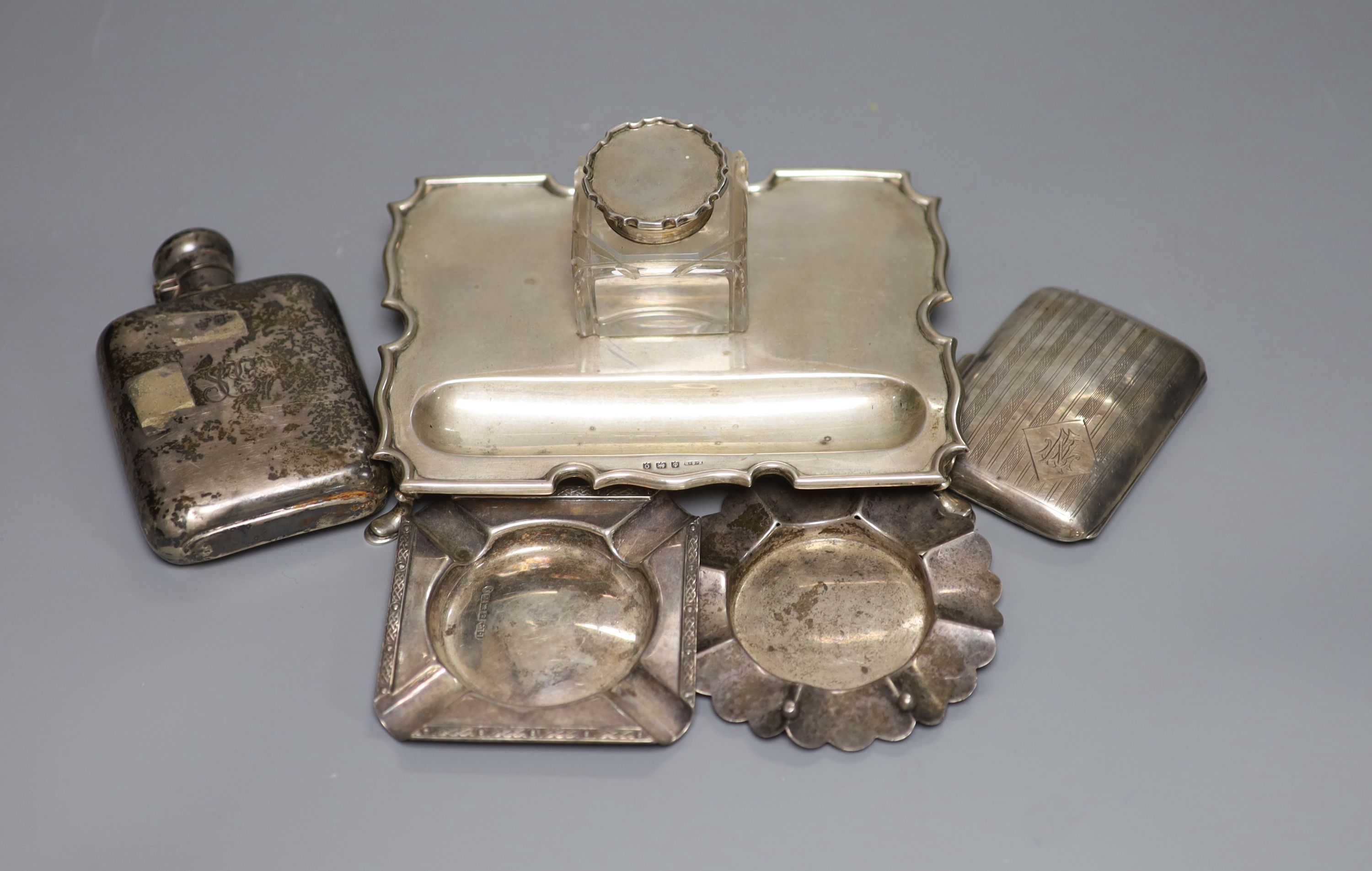 A silver shaped rectangular inkstand, fitted a silver-mounted cut glass bottle, a silver hip flask, engine-turned cigarette case and two ashtrays 13.5oz approximately